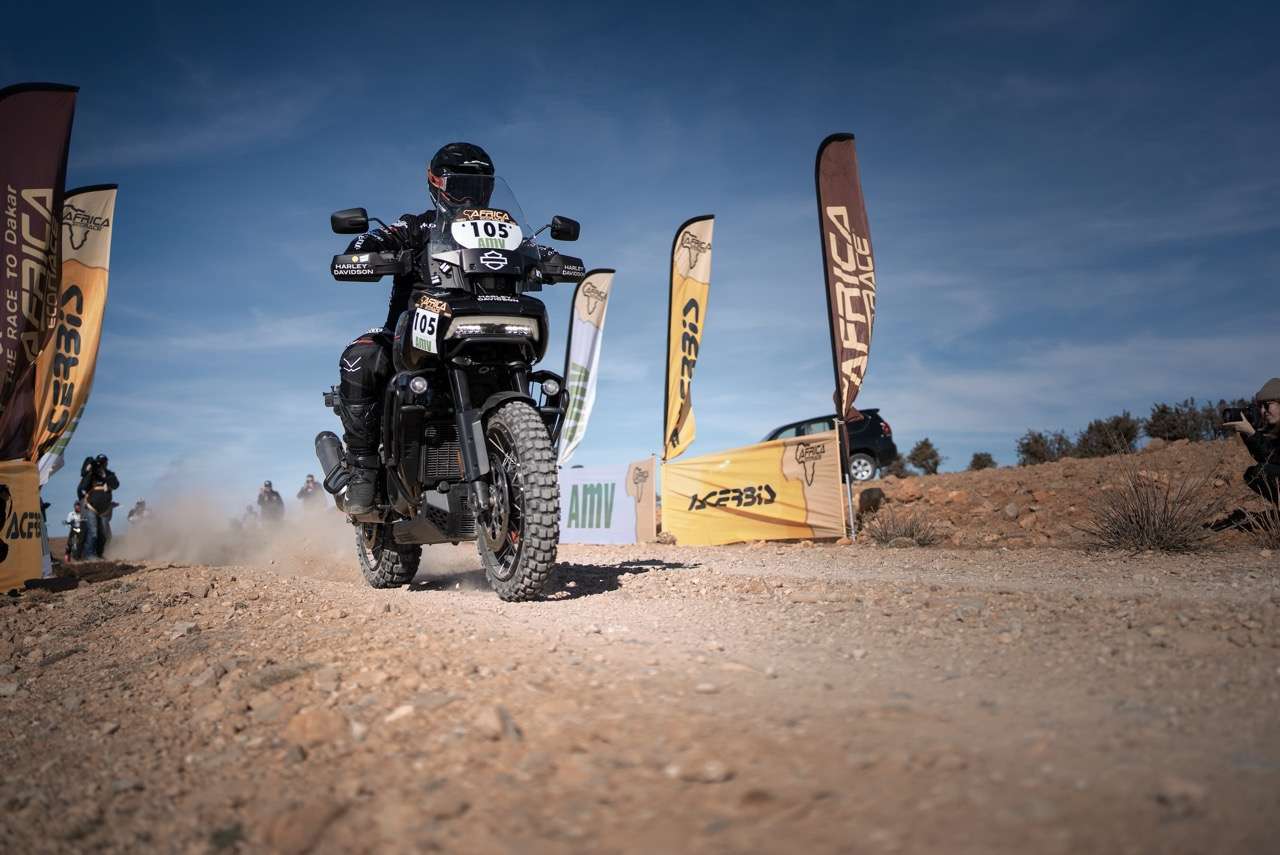 Joan Pedrero rides the Harley-Davidson Pan America 1250 through the desert in the Africa Eco Race 2025, surrounded by sand dunes and clear skies.