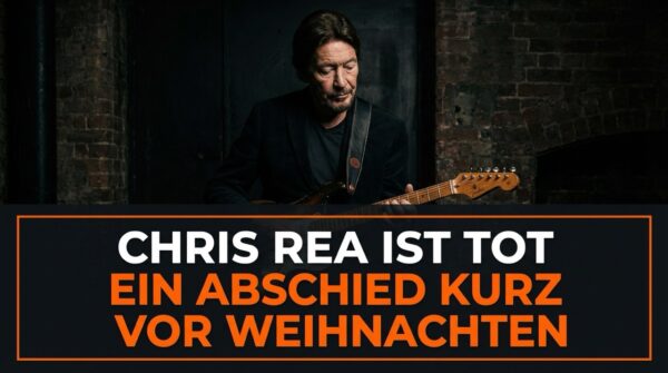 Zu sehen ist Chris Rea mit einer E-Gitarre, in ruhiger, nachdenklicher Haltung. Das Bild ist dunkel gehalten, mit warmen Lichtakzenten und einem reduzierten Hintergrund aus Backstein. Der Fokus liegt klar auf der Person und dem Instrument.