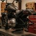 Harley-Davidson Softail auf der Werkstattbühne mit sichtbarem Antrieb und Werkzeugwand im Hintergrund.